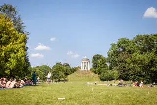 Münchner genießen die Sonne auf der Wiese unter dem Monopteros im Englischen Garten