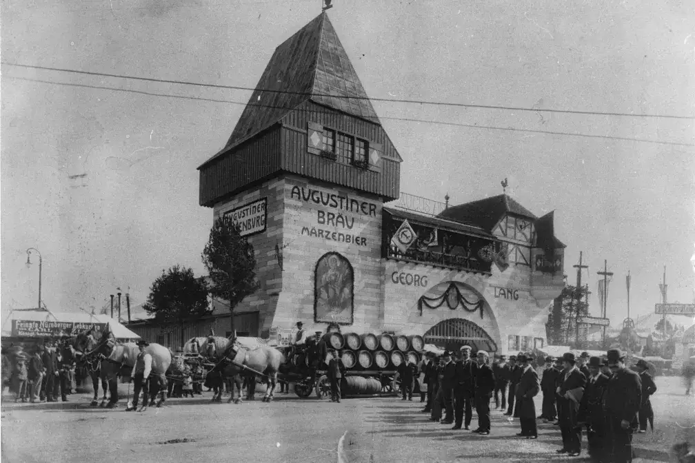 Oktoberfest 1910: Die "Bierburg", das Augustiner Bräu, von Georg Lang auf der Oktoberfestwiese. Davor ein vierspanniges Bierfuhrwerk und Festbesucher.