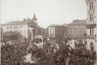Faschingswagen "Zum Kamin", von Pferden gezogen, auf dem Bahnhofsplatz beim Faschingszug 1896. Eher wie eine riesige Dampflok sieht dieser Faschingswagen beim Umzug 1896 aus. Passend dazu trägt er den Titel "Zum Kamin" und wird natürlich nicht von Dampf angetrieben, sondern von Pferden gezogen. Das Foto zeigt den Wagen auf dem Bahnhofsplatz von zahlreichen Zuschauern umgeben.