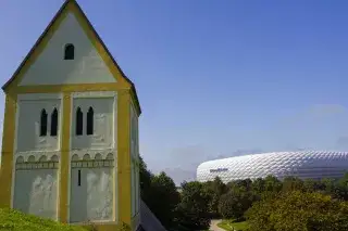 Die Heilig-Kreuz-Kirche in Fröttmanning mit der Allianz Arena im Hintergrund