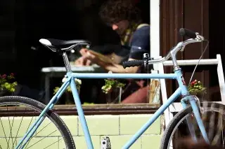 Fahrrad lehnt abgesperrt an einer Wand vor einem Laden.