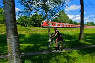 Fahrradfahrer im Grünen mit Zug im Hintergrund