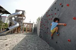 Kind spielt an einer Kletterwand im Spielplatz im Heckenstallerpark. Kind spielt an einer Kletterwand im Spielplatz im Heckenstallerpark.