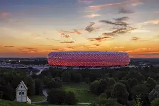 Die Allianz Arena leuchtet in den Farben des FC Bayern in der Abenddämmerung