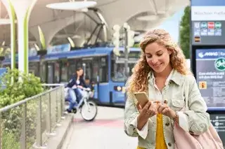 Frau an einer Haltestelle schaut aufs Handy