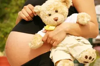 Eine hochschwangere Frau hat einen Teddy im Arm