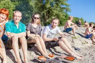 Vier Personen sitzen an der Isar in München und grillen Vier Personen sitzen an der Isar in München und grillen