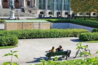 Ein Paar sitzt auf einer Bank und genießt die Sonne vor der Bayerischen Staatskanzlei Ein Paar sitzt auf einer Bank und genießt die Sonne vor der Bayerischen Staatskanzlei
