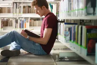 Ein junger Mann liest in einem Buch in einer Bibliothek