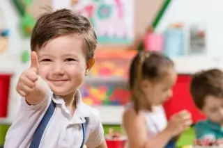 Kind Kita Daumen Ein Kind spielt in der Kinderbetreuung und zeigt den Daumen nach oben