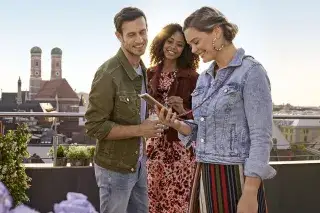 Ein Mann und Frauen stehen auf einer Dachterrasse vor dem Panorama von München Ein Mann und Frauen stehen auf einer Dachterrasse vor dem Panorama von München