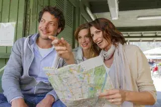 Ein Mann und zwei Frauen blicken auf dem Viktualienmarkt auf einen Stadtplan