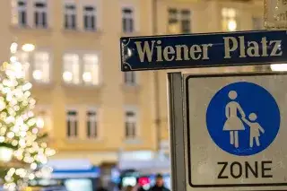 Ein Straßenschild am Wiener Platz bei Dunkelheit, im Hintergrund ein beleuchteter Christbaum