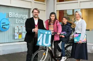 Die ehemalige Bürgermeisterin Katrin Habenschaden und Sportreferent Florian Kraus posieren mit zwei Kindern und einem Fahrrad bei der Übergabe der Upcycling-Materialien.