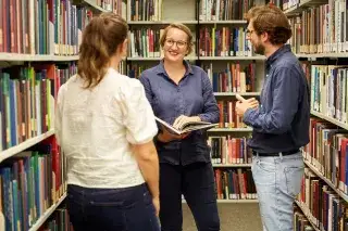 Drei Personen unterhalten sich in der Bibliothek Drei Personen unterhalten sich in der Bibliothek