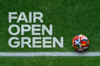 Weiße Schrift auf grünem Rasen mit den Worten Fair, Open, Green und einem Fußball
