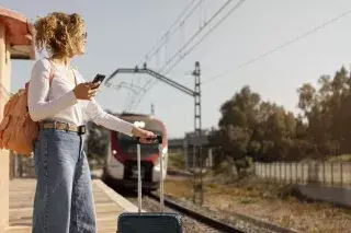 Frau mit Handy und Koffer wartet auf einen Zug