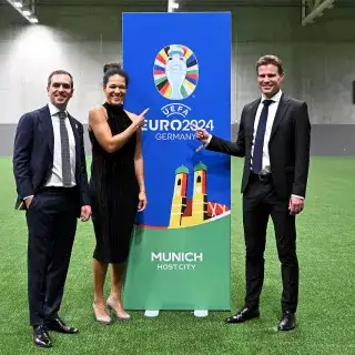 Turnierdirektor Philipp Lahm, Botschafterin Celia Šašić und Botschafter Felix Brych posieren mit einem Banner für die Host City München bei der Fußball-EM 2024