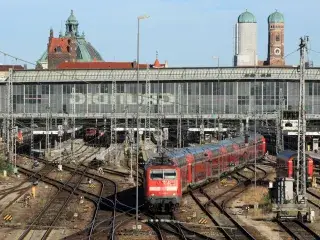 Eine rote Lok mit einem Regionalexpress fährt auf den Gleisen aus der Haupthalle des Münchner Hauptbahnhofs