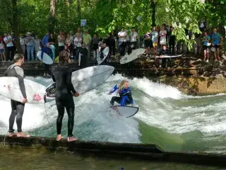 Eine Surferin reitet die Eisbachwelle im Lehel