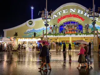 Regen auf der Wiesn am Abend: Gäste mit Schirmen vor der Ochsenbraterei