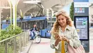 Frau an einer Haltestelle schaut aufs Handy