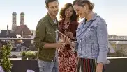 Ein Mann und Frauen stehen auf einer Dachterrasse vor dem Panorama von München