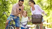 Vater, Mutter und Kind stehen mit ihrem Fahrrad und schauen auf ein Smartphone