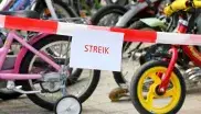 Zettel mit dem Wort "Streik" an einem Absperrband vor Kinderfahrrädern